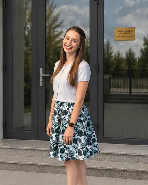 Mišić Ioana-Cristiana, logoped pentru copii, zâmbind în fața intrării cabinetului său de logopedie din Timișoara