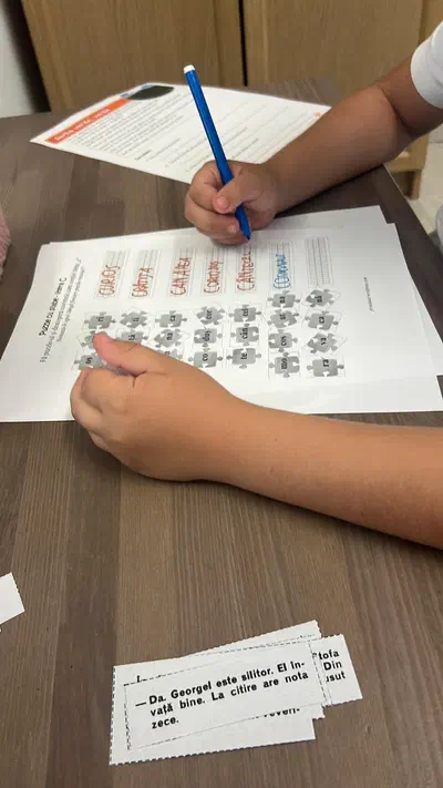 Copil scriind cu creionul și completând o fișă cu puzzle de silabe la cabinetul de logopedie din Timișoara