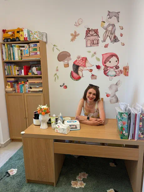 Mišić Ioana-Cristiana, logoped pentru copii, la biroul din cabinetul ei din Timișoara, cu rafturi de cărți și jocuri în spate